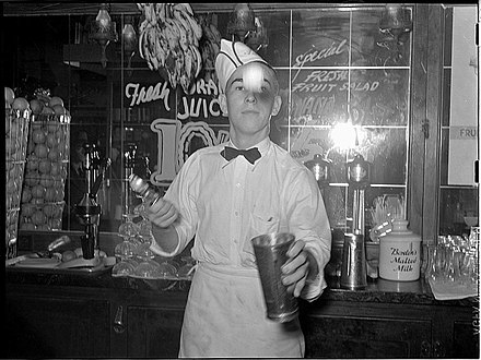 A soda jerk tossing a scoop of ice cream into a metal mixing cup before blending a malted shake, Texas, 1939