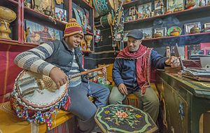 Deux hommes assis autour d'une table basse, celui de gauche jouant du guembri.