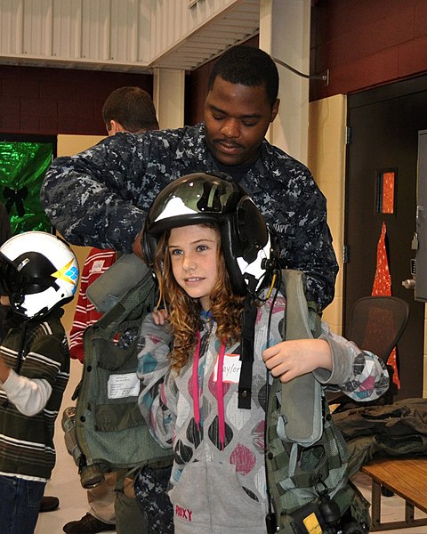File:US Navy 091209-N-6999T-001 Parachute Rigger 3rd Class Donte Nickerson helps a little girl try on a survival vest.jpg