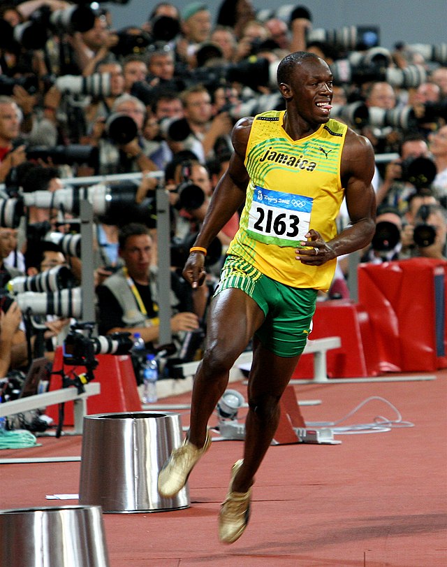 Usain Bolt in a yellow running vest and green shorts just completing a race