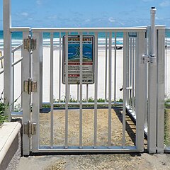Beachside gate with a self-latching device and a higher than 54” release mechanism.