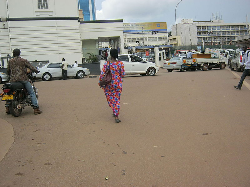 File:A woman in a kitengi on a street holding a bag.JPG