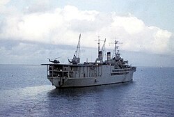 USNS Corpus Christi Bay (T-ARVH-1) at anchor off Vung Tau, South Vietnam, circa 1967–1969. A pair of UH-1 Huey helicopters sit atop her aft flight deck.