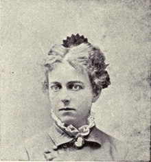 An 1892 image of a white woman with light hair in an updo; she is wearing a high-collared blouse and jacket