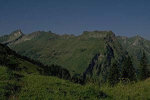 Berggächtle (a majdnem ugyanolyan magas hegygerinc bal sarka) a Roßkopf felől.  Tőle jobbra (a kép jobb szélén a három lucfenyőtől balra lévő hegy) az oromzat.  Távol balra a kép szélén a csiga.