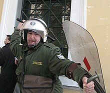 A Greek riot policeman wielding a baton towards an Athens Indymedia photographer during a protest at courts in Athens, Greece Greek riot police reverse baton 12-3-07.jpg