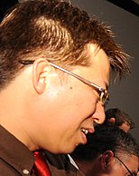 Profil d'un homme de type asiatique, souriant, portant des lunettes.