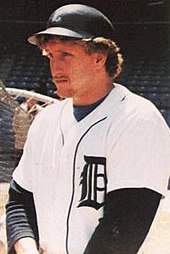 A baseball player is shown waist up with a batting helmet on his head.