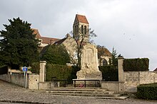 Monument aux morts de Luzarches, en commémoration de la Première Guerre mondiale, dessiné par l'architecte Naudin ; au fond, l'église paroissiale.