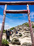 Kleurenfoto: close-up van een torii, de poort naar een shinto-heiligdom, bovenop een met rotsen bezaaide berg, onder een bewolkte blauwe lucht.