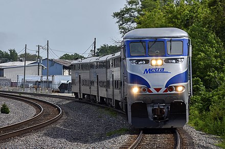 An outbound Metra train approaches the Schiller Park station in June 2019, being led by an Ex-Amtrak EMD F59PHI.
