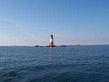 Vue d’un phare sur un îlot rocheux, au milieu de la mer.