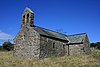 Eine einfache Steinkirche mit einem Schieferdach, einem Glockenturm am nächsten Giebel und einem Querschiff rechts