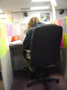 Telemarketing agent sitting in a cubicle. The brightly colored rebuttal sheets are used to answer most questions a customer might have. Telemarketerjohn.jpg