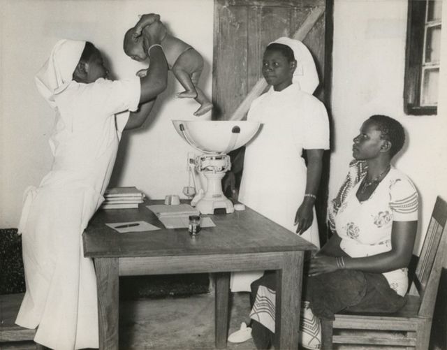 Tanzanian midwife weighing an infant and giving advice to the mother