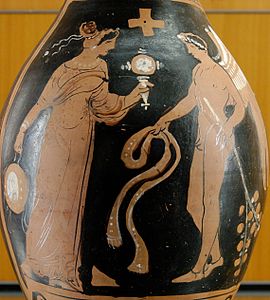 Woman holding a mirror and a tambourine facing a winged genie with a ribbon and a branch with leaves. Ancient Greek red-figure oinochoe, ca. 320 BC, from Magna Graecia. (Notice the coloured decorative woven stripes hanging on the tambourine, which can still be seen today on "tamburello", the tambourine of Southern Italy.)