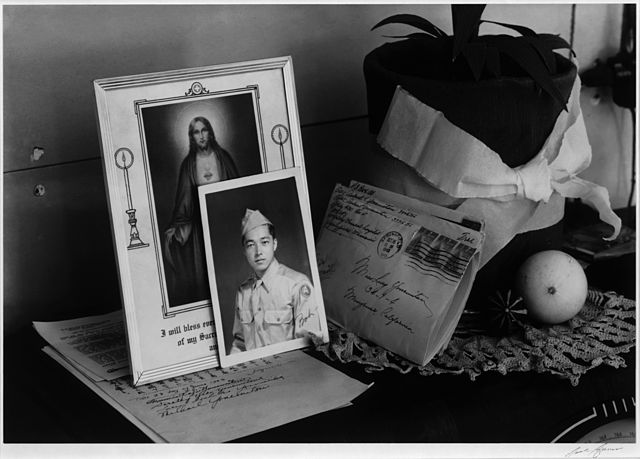 A homemade planter and a doily beside a service portrait, a prayer, and a letter home. One of the few ways to earn permission to leave the camps was t