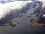 Luftaufnahme einer an einem Fjord in bergiger Umgebung gelegenen Ortschaft