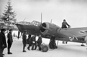 A Finnish bomber plane is being refueled by hand by six servicemen at an air base on a frozen lake.