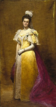 Brown-haired woman in 19th-century period long yellow dress with purple train in front of a brown backdrop