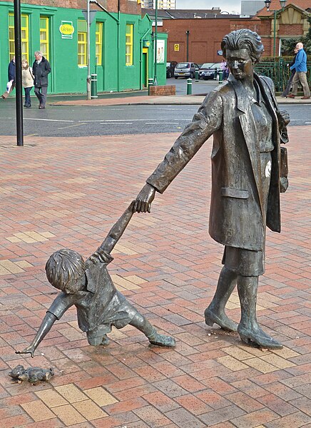 Sculpture of a grandmother walking and holding her grandchild's hand while leans over to reach for a dropped teddy bear.