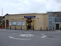 A beige-bricked building with a rectangular, blue sign reading "HIGH BARNET STATION" in white letters all under a blue sky with white clouds
