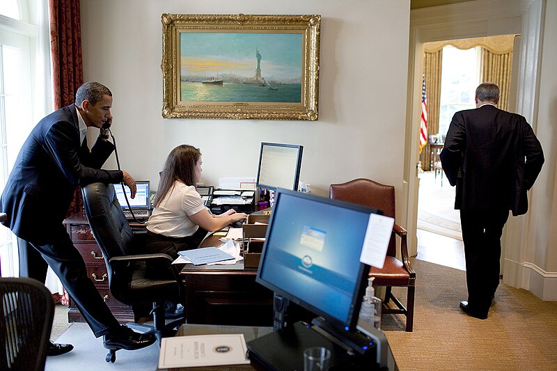 File:President Barack Obama talks on the phone with a Member of Congress, while Katie Johnson, the President's personal secretary, works at her desk in the Outer Oval Office.jpg