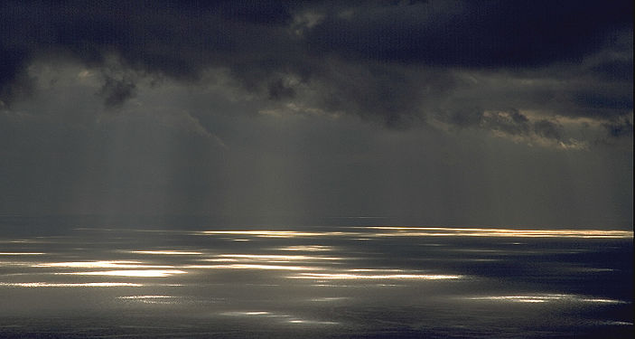 Sunrays through thick clouds draw patches of light onto the Atlantic Ocean off Madeira's south coast.