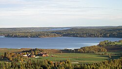 Utsikt från Kasberget mot havet med byn Flor och Florsjön i förgrunden. Sommarbild med gröna åkrar och blått vatten.