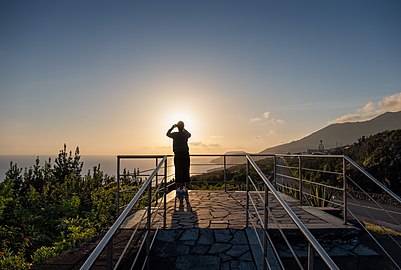 Woman photographing the sunset at the 'Pôr-do-Sol' scenic viewpoint, São Jorge, Azores, Portugal