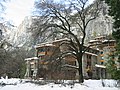 Фотография Ahwahnee в зимнем снегу, среди голых деревьев с впечатляющими стенами долины Йосемити, возвышающимися позади.