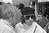 Jackie Stewart sağındaki başka bir adam onunla konuşurken kameranın soluna bakıyor