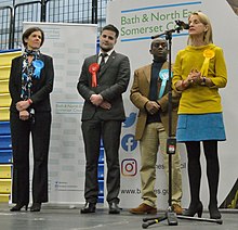 An election declaration for the UK 2019 general election, with four candidates wearing rosettes. Left to right: Conservative, Labour, Brexit, Liberal Democrat Candidates, Bath 2019 general election declaration of results (cropped).jpg