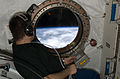 Astronauta observa a Terra através da escotilha do módulo Kibo.