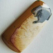 A freeform cabochon of Ohio flint with a pattern of cream and ochre bands and a bluish black pattern at one end.