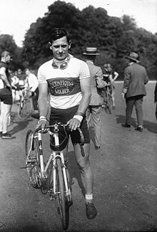 Portrait en noir et blanc d'un cycliste tenant son vélo à côté de lui, vêtu d'un maillot blanc.