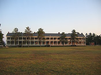 The Barracks as viewed from the parade ground. The surviving brick powder magazine from the same era and the "old post cemetery" beyond can be seen just to the right. OldStoneBarracksFront.jpg