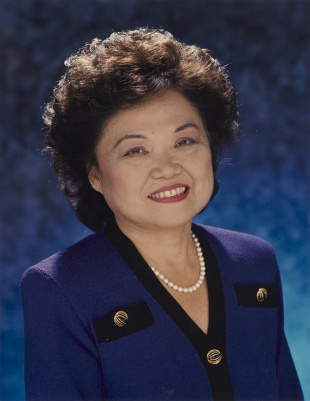Portrait of a woman in a blue suit adorned with a pearl necklace