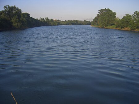 A ميلddle-sized river flows placidly between banks covered in vegetation.