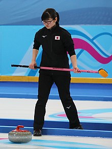 Momoha Tabata holds a broom while looking down at a curling stone