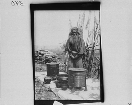 File:Ainu man standing outdoors on a mat covered with clay containers LOC agc.7a10195.tif