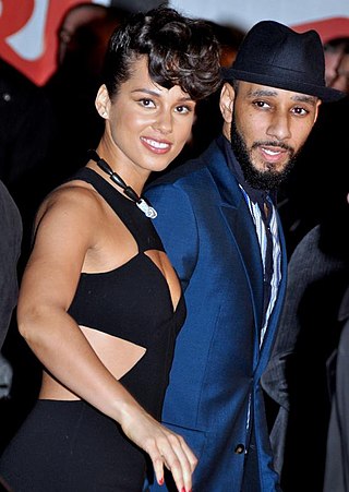 A woman wearing a black dress and a man wearing a suit look toward a camera