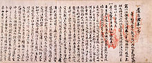 Photo couleur d'un texte écrit sur du papier en caractères chinois noirs sur fond rose, avec deux empreintes de mains en rouge à droite.