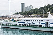 Photographie d'un ferry sur lequel il est écrit « Labuan Express 2 ». À l'arrière-plan se trouvent deux gratte-ciels.