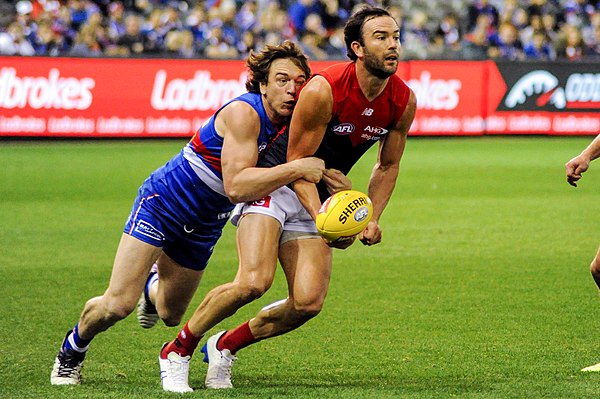 Western Bulldogs player Liam Picken tackling Jordan Lewis of Melbourne, who is attempting a handball