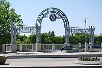 A cast iron triple arch about four metres in height and painted white. The words "Progress" and "Prosperity" can be seen above the left and right arches respectively.