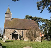 Een stenen kerk met een pannendak vanuit het zuiden gezien.  Aan de linkergevel is een shingled bellcote, en een houten veranda steekt uit de kerk