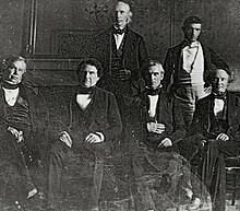 Polk and his cabinet in the White House dining room, 1846. Front row, left to right: John Y. Mason, William L. Marcy, James K. Polk, Robert J. Walker. Back row, left to right: Cave Johnson, George Bancroft. Secretary of State James Buchanan is absent. This was the first photograph taken in the White House, and the first of a presidential Cabinet. State-dining-room-polk-cabinet.jpg