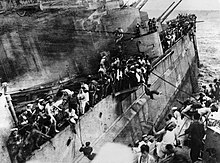The crew of the sinking Prince of Wales abandoning ship to the destroyer Express. Moments later, the list on Prince of Wales suddenly increased and Express had to withdraw. Observe the barrels of the 5.25 in guns, which were unable to depress far enough to engage attackers due to the list. The Sinking of HMS Prince of Wales by Japanese Aircraft Off Malaya, December 1941 HU2675.jpg