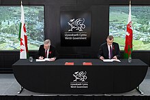 Welsh Labour leader Mark Drakeford and Plaid Cymru leader Adam Price sign the agreement, December 2021 Wales Co-operation Agreement 1.jpg